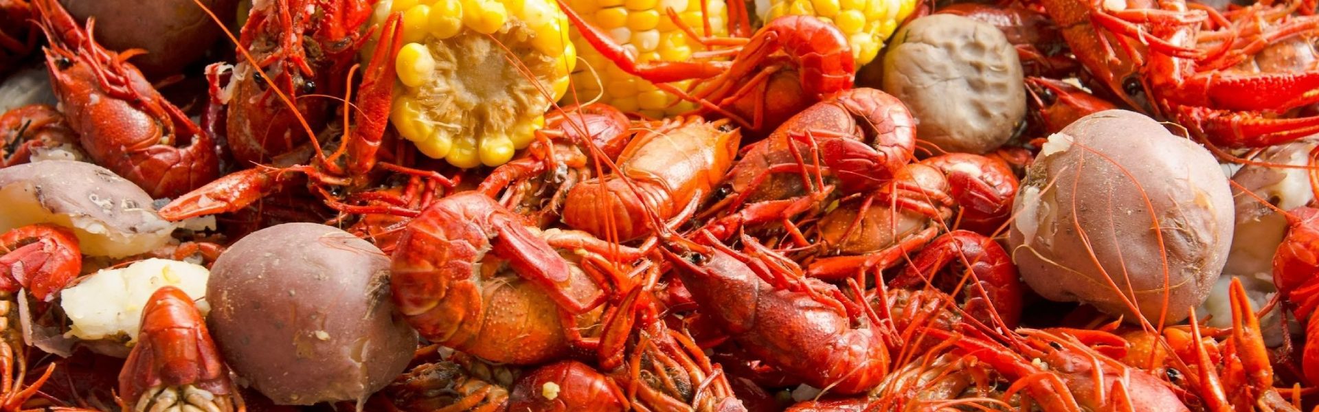 A pile of crawfish next to corn on the cob.